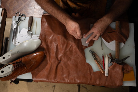 Skilled craftsman sewing leather with tools on a worktable, shoemaking in progress in a workshop...