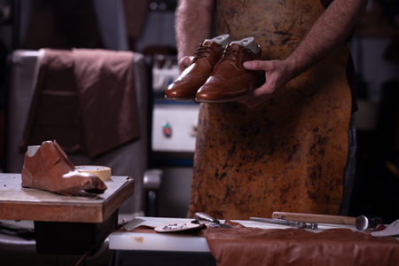 Shoemaker holds polished brown leather shoes in a workshop during a crafting session