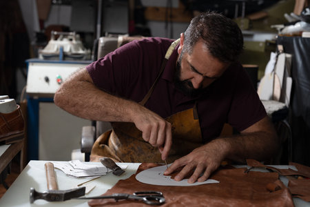 Skilled craftsman carving leather at a worktable with tools and leather scraps nearby