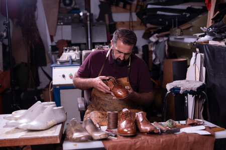 Shoemaker at work crafting leather shoes in a busy workshop with tools and scraps todayの写真素材