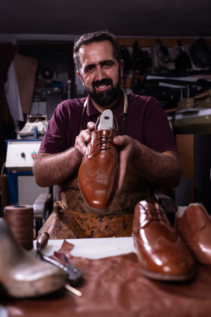 Cobbler in workshop presenting brown leather dress shoe with pride and craftsmanshipの写真素材