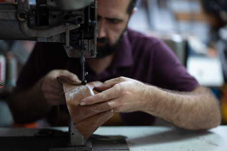 Leather worker hand sewing a leather piece on an industrial sewing machine in a workshopの写真素材