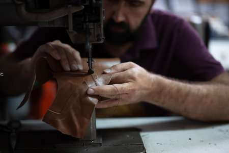 Leather work in progress: skilled craftsman sewing brown leather piece with industrial sewing machineの写真素材
