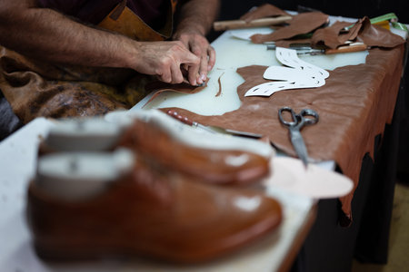 Leather craftsman at work shaping leather with tools and patterns on a workshop table