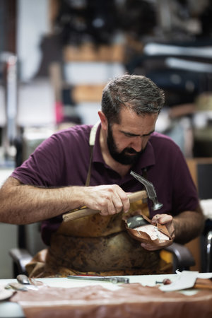 Craftsman hammering a leather shoe in a busy workshop, focusing on handmade footwearの写真素材