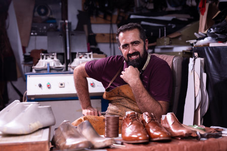 Shoemaker in a leather workshop, smiling at his bench with polished brown shoes