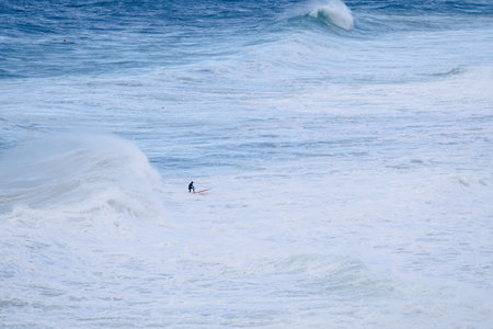 Surfer riding a massive ocean wave in a vast blue seascape at sea
