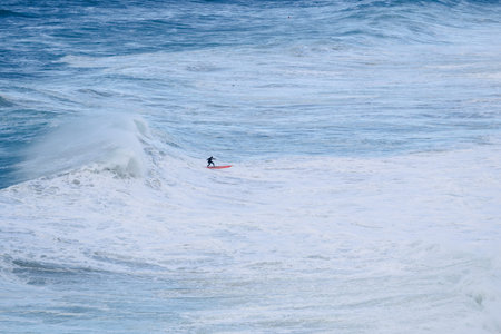 Surfer rides a dramatic big wave on a red board in the open blue ocean