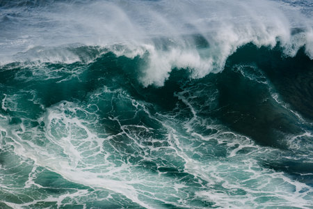 Massive ocean wave curling and crashing with white foam over dark teal water in motion