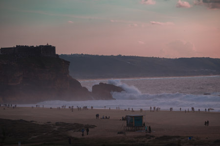 Evening on the beach with waves, cliffs, and a fortress overlooking a busy shorelineの写真素材