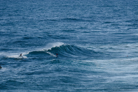 Surfers ride a powerful blue ocean wave, capturing intense motion and sport in the open sea