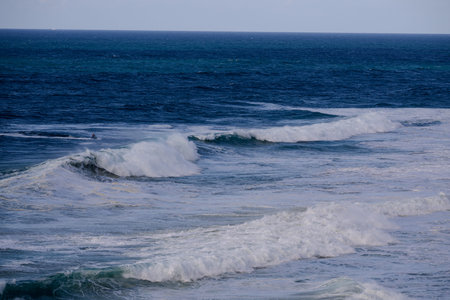 Powerful ocean waves crash on the shore under a deep blue sea and clear sky