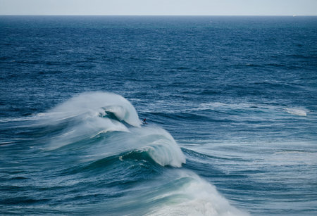 Powerful ocean waves with surfers riding a breaking barrel under a clear blue skyの写真素材