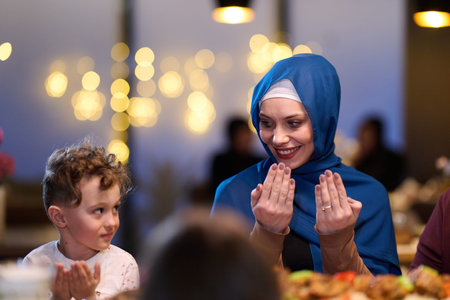 Muslim Mother and Son Praying Before Iftar Meal at Home or Restaurant - Religious Traditions, Ramadan Kareem, and Family Bonding Concept.の写真素材