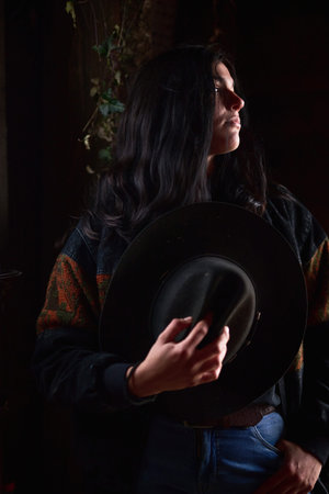 Moody portrait of a woman holding a wide brim hat in a dimly lit settingの写真素材