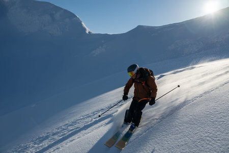 Skier carving down a sunlit powder slope on a rugged mountain during a winter adventure