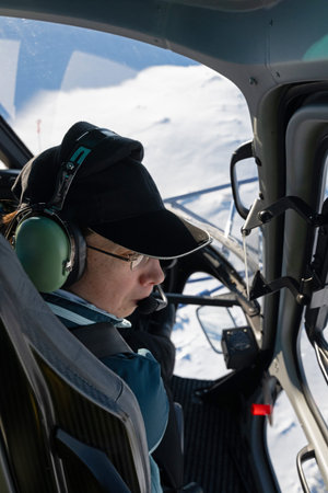 Pilot in cockpit wearing headset in snow-covered landscape, winter flight over pristine white...