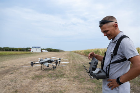 Drone pilot with remote controller in a farmland field beside a ready quadcopterの写真素材