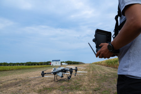 Drone pilot prepares controller while drone rests in a rural agricultural field under a blue skyの写真素材