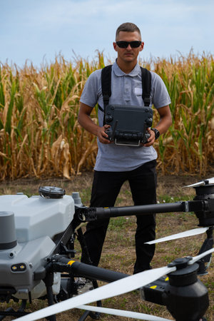 Drone pilot operating an agricultural drone in a cornfield with remote controller and safety gearの写真素材