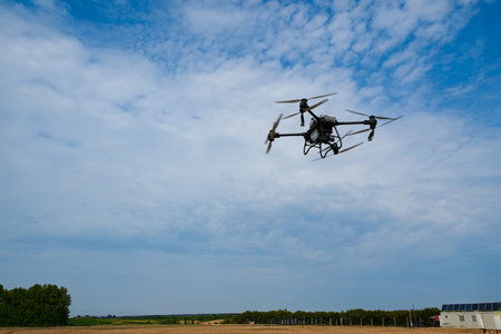 Drone in flight over open fields on a clear day with a distant farm buildingの写真素材