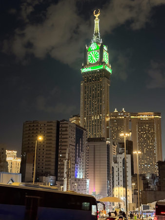 Night view of Abraj Al Bait clock tower in Mecca with illuminated green clock and city skyline
