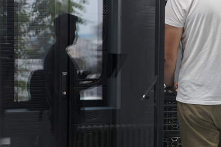 IT technician working on server rack in data center with reflected colleague through glass