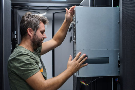 It technician installing server hardware in a data center rack performing maintenance and network...