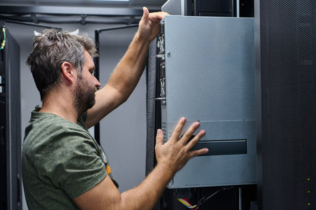 It technician installing a server in a data center rack performing hardware maintenance and network...