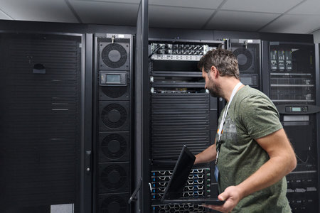 IT technician inspecting server rack in a data center with laptop during maintenance