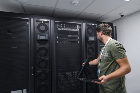IT technician checking servers in a modern data center server room with laptop and racks