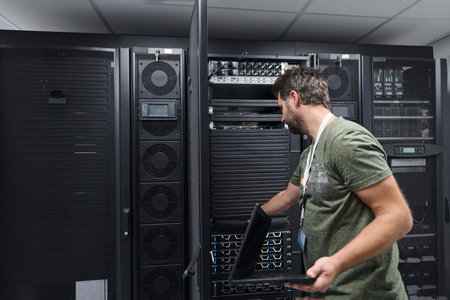 IT technician working on servers in a data center with laptop performing maintenance and monitoring