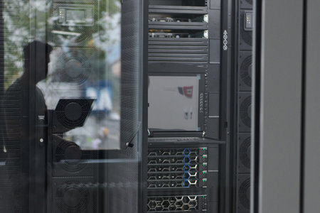 Data center server racks and monitoring equipment reflected in glass with technician working in...