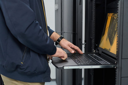 Data center technician using laptop on rack-mounted console to manage servers and network equipment