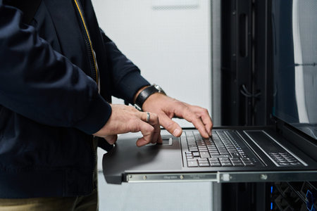IT technician typing on a laptop in a server rack in a data center performing network maintenance