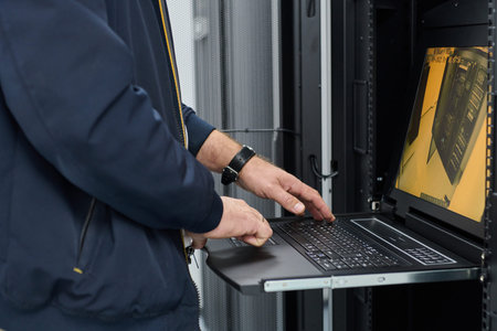 IT technician working on server rack using laptop console in data center for system maintenance and...