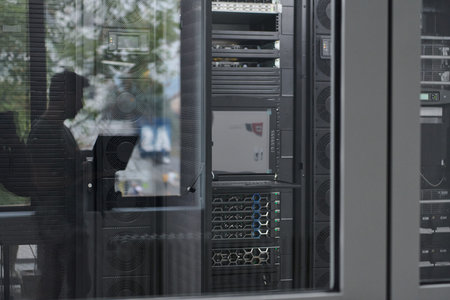 Data center server racks and network equipment reflected in a glass door with silhouetted technician