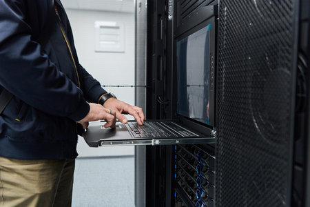 IT technician working on laptop in server rack during data center maintenance and network...