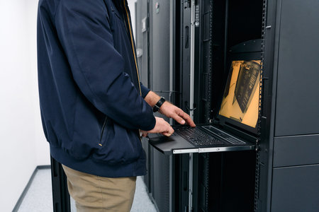 IT technician working on laptop inside a server rack in a data center maintenance room