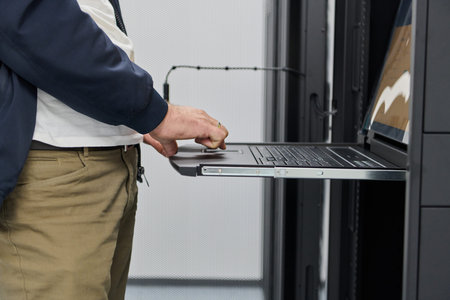 IT technician using a rack-mounted laptop console in a data center server rack for maintenance and...