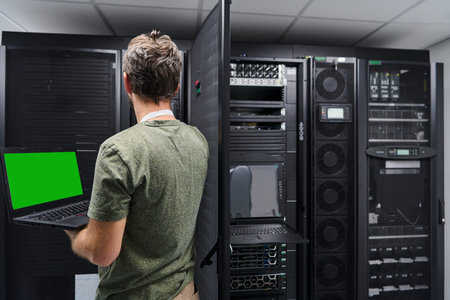 Data center technician using laptop to check server rack and network equipment in a server room