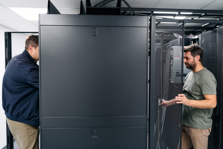 Two IT technicians working on server racks in a data center performing maintenance and hardware...