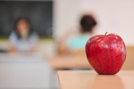 Red apple on a school desk in a classroom with blurred students and teacher in the background