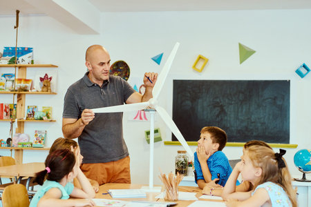 Teacher demonstrates a model wind turbine to elementary students during a hands-on STEM classroom...