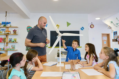 Teacher and elementary students exploring a model wind turbine during a hands-on classroom science...