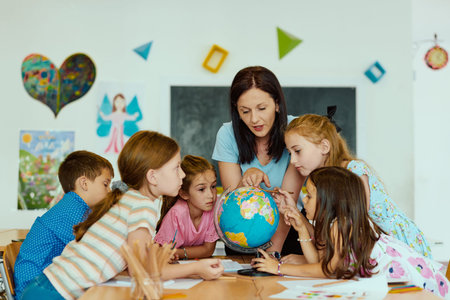 Teacher showing globe to curious elementary students gathered around a table in colorful classroom