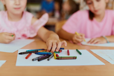 Children reaching for colorful crayons while drawing together at a classroom table