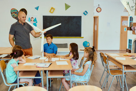 Teacher demonstrates wind turbine model to attentive children in a primary classroom science lesson