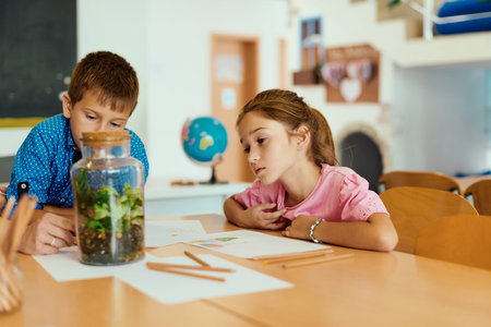 Two curious children examining a glass terrarium while drawing and learning together in a classroom