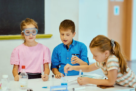 Three children doing a science experiment at school table, learning and collaborating in a classroomの写真素材